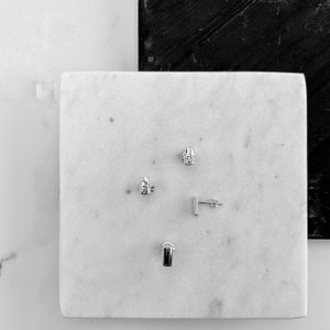 May include: Four silver earrings on a white marble surface. The earrings are all different shapes and sizes.