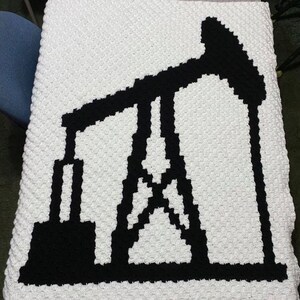 May include: A white crocheted blanket with a black silhouette of an oil derrick.