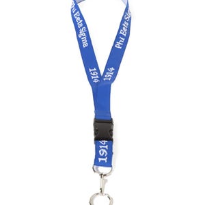 May include: A blue lanyard with white text that reads "Phi Beta Sigma" and "1914". The lanyard has a black plastic clasp and a silver-colored metal clip and ring.