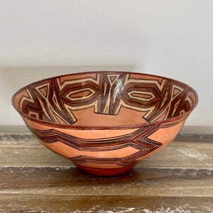 May include: A terracotta bowl with a geometric pattern in brown and orange. The bowl is hand-painted with a unique design.