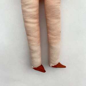 May include: A pair of cream-colored fabric legs with brown fabric feet. The legs are sewn together at the top and the feet are sewn to the bottom of the legs.