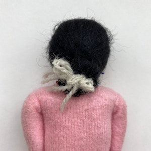 May include: A handmade doll with black hair tied with a white ribbon, wearing a pink sweater.
