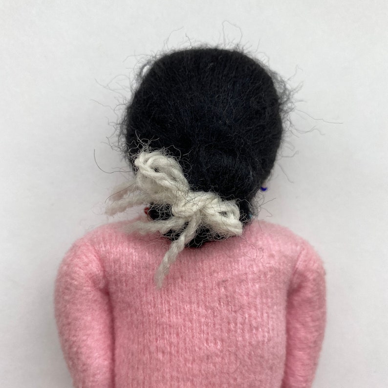 May include: A handmade doll with black hair tied with a white ribbon, wearing a pink sweater.