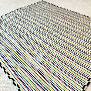 May include: A colorful quilt with a white background and vertical stripes in red, yellow, green, blue, and black. The quilt has a black and white checkered border on one side.