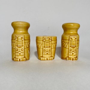 May include: Three ceramic salt and pepper shakers with a Mayan-inspired design. The shakers are in shades of brown and feature intricate carvings of human figures.
