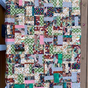 May include: A patchwork quilt with a variety of colorful fabrics, including green, pink, red, and blue. The quilt is made up of squares and rectangles of different sizes and patterns.