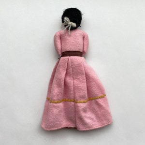 May include: A pink fabric doll with black hair, a brown belt, and gold trim on the skirt.
