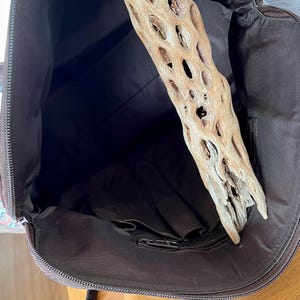 以下が含まれることがあります： ジッパー付きの茶色のキャンバス地のトートバッグの内側。バッグには内側に大きなポケットがあり、流木がバッグの中に置かれています。