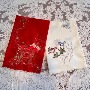 May include: Two embroidered Christmas tablecloths, one red with a floral design and the other white with a snowman design.