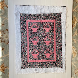 May include: A quilt block with a pink and black floral pattern. The block is made up of six smaller blocks, each with a different design. The block is surrounded by a pink border.