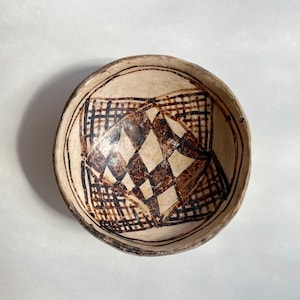 May include: A white ceramic bowl with a brown geometric design. The design features a central diamond shape surrounded by a grid pattern.