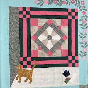 May include: A quilt with a green, pink and white patchwork design. The quilt features a floral vine border and a cat applique in the bottom left corner.