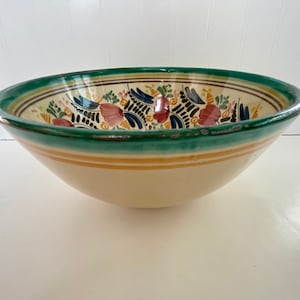 May include: A large, white ceramic bowl with a green rim and a colorful floral design. The bowl has a wide, shallow shape and is perfect for serving salads, pasta, or fruit.