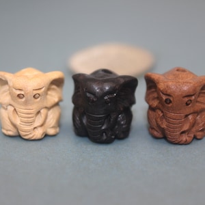 May include: Three wooden elephant figurines, one natural wood color, one black, and one brown. The elephants are carved in a sitting position with their trunks curled up.
