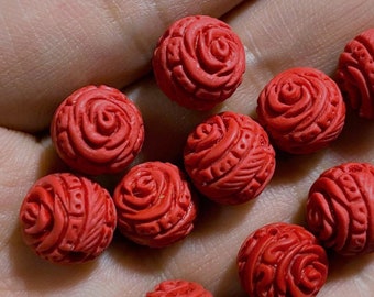 Può includere: Una collezione di dieci perle rotonde rosse con un design a rosa. Le perle sono realizzate in un materiale liscio e lucido e hanno una superficie leggermente strutturata.
