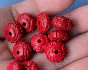 Può includere: Primo piano di una mano che tiene un mucchio di perline rotonde rosse con intagli intricati. Le perline sono fatte di un materiale liscio e lucido.