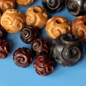 May include: A collection of wooden beads with intricate carved designs. The beads are in shades of brown, black, and natural wood.