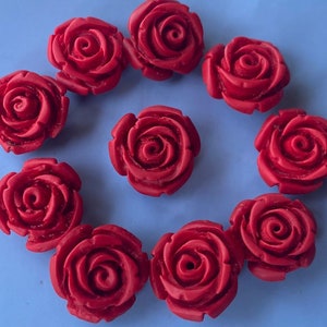 Può includere: Dieci decorazioni in resina a forma di rosa rossa con un design tridimensionale dettagliato. Le rose sono disposte in cerchio su uno sfondo blu.
