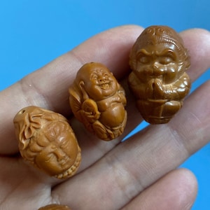 Może przedstawiać: Kolekcja małych, misternych drewnianych figurek przedstawiających uśmiechnięte, siedzące postacie. Figurki są jasnobrązowe i mają szczegółowe rysy twarzy.