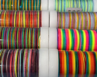 Könnte beinhalten: Eine Sammlung bunter Armreifen in verschiedenen Farbtönen von Rot, Orange, Gelb, Grün, Blau, Lila und Rosa. Die Armreifen sind in durchsichtigen Plastikröhren mit weißen Kappen gestapelt.