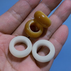 Könnte beinhalten: Vier glatte, runde Ringe, zwei weiße und zwei braune, werden in einer Hand gezeigt. Die Ringe sind aus einem polierten Material, möglicherweise Stein oder Keramik.
