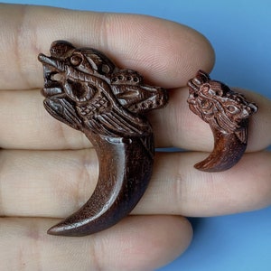 Puede incluir: Dos tallas de madera de cabezas de lobo, una más grande que la otra, con detalles intrincados y un color marrón oscuro.