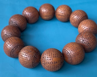 May include: A brown wooden bracelet with 18 beads, each engraved with intricate patterns and characters. The bracelet is laid out on a blue surface.