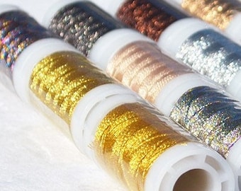 May include: A set of eight spools of metallic embroidery thread in various colors, including gold, silver, black, and iridescent. The spools are arranged in a row, with the ends of the thread visible.
