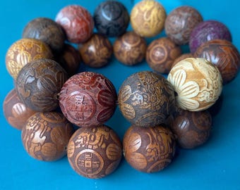 May include: A collection of intricately carved wooden beads in various shades of brown, red, and cream. Each bead features detailed patterns and designs, showcasing a range of textures and styles. The beads are arranged on a blue surface.