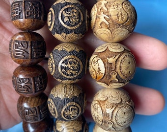May include: Close-up of a wooden beaded bracelet. The beads are carved with intricate designs, including Chinese characters and circular patterns. The beads are various shades of brown and tan.