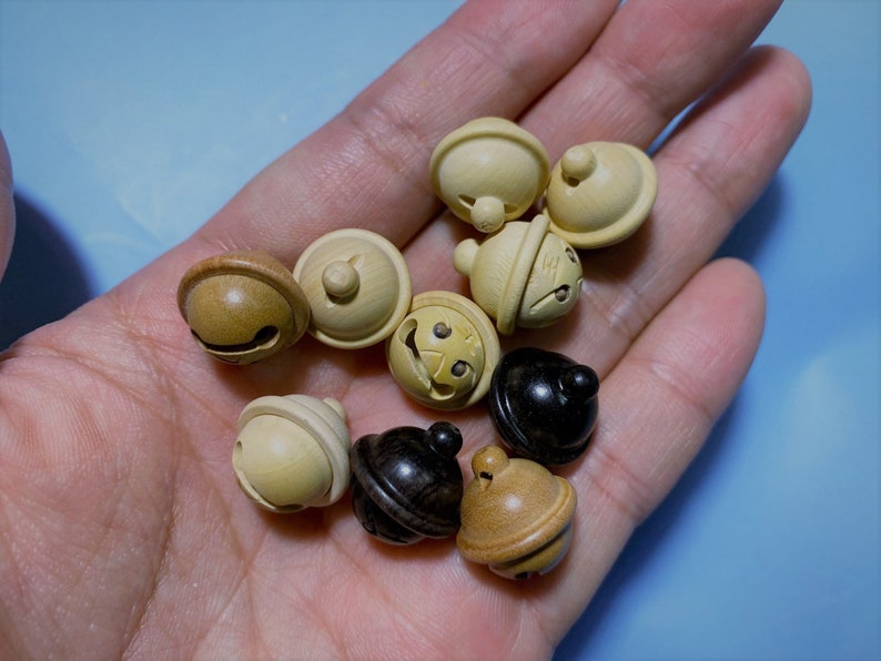 K&ouml;nnte beinhalten: Eine Sammlung von Holzklingeln in verschiedenen Braunt&ouml;nen und Beige. Einige Klingeln haben eine glatte Oberfl&auml;che, w&auml;hrend andere eine strukturierte Oberfl&auml;che haben. Die Klingeln sind klein und haben oben ein Loch zum Aufh&auml;ngen.