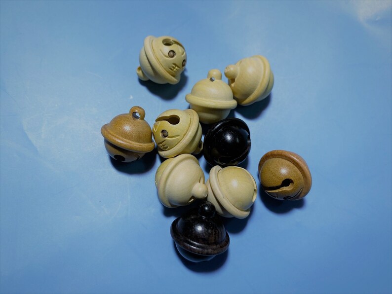 K&ouml;nnte beinhalten: Eine Sammlung von Holz- und schwarzen Gl&ouml;ckchen in verschiedenen Braunt&ouml;nen und Cremefarben. Die Gl&ouml;ckchen sind in einer Gruppe auf einem hellblauen Hintergrund angeordnet.