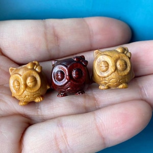 Può includere: Tre statuette di gufo in legno, ognuna con uno schema di colori diverso. Una è marrone e gialla, un'altra è marrone e rossa e l'ultima è marrone e bianca.
