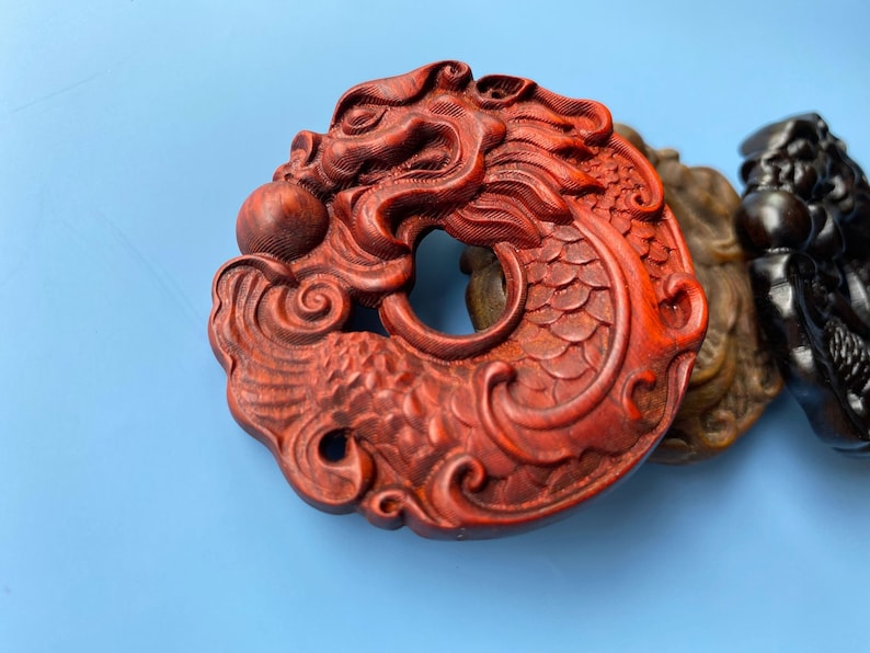K&ouml;nnte beinhalten: Eine rote Holzschnitzerei eines Drachen mit aufwendigen Details. Der Drache ist um einen Kreis gewickelt und hat eine Perle im Maul.