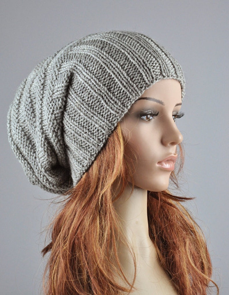 May include: A gray slouchy beanie hat made of knitted wool. The hat is soft and comfortable and has a relaxed fit.