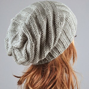 May include: A gray slouchy beanie hat with a ribbed texture. The hat is made of a soft, knitted fabric.