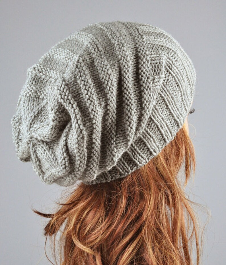 May include: A gray slouchy beanie hat with a ribbed texture. The hat is made of a soft, knitted fabric.