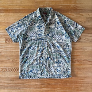 Peut inclure: Une chemise à manches courtes boutonnée avec un motif patchwork répétitif dans des tons de bleu, vert et blanc. Le design comprend diverses formes géométriques, des motifs floraux et des lignes abstraites sur toute la surface.