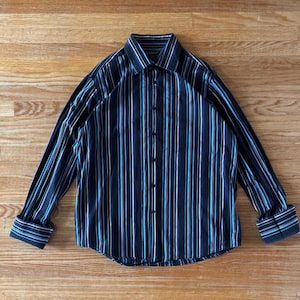 May include: A long-sleeve button-down shirt featuring a dark navy blue base with vertical stripes in shades of light blue, white, and thin orange. The shirt includes a pointed collar, a front button placket, and cuffs with button closures.