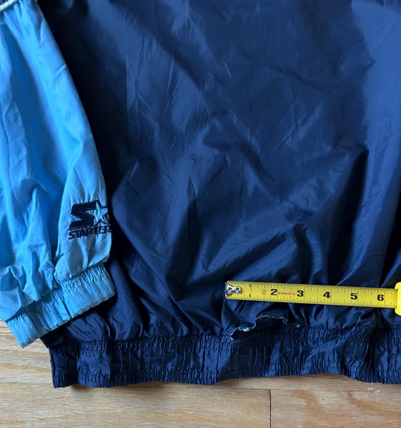 May include: A navy blue and light blue Starter jacket. The jacket has a drawstring waist and elastic cuffs. The Starter logo is visible on the light blue sleeve. The jacket is approximately 6 inches wide.