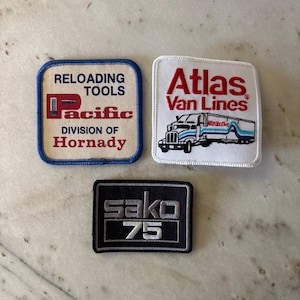 May include: Three embroidered patches: a square off-white patch with blue border reading 'RELOADING TOOLS Pacific DIVISION OF Hornady', a square white patch with 'Atlas Van Lines' and a truck graphic, and a black rectangular patch reading 'sako 75'.