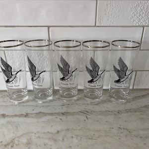 May include: A white ceramic mug with a black handle and the text "But First, Coffee" in a black, handwritten-style font. The mug is on a white surface.