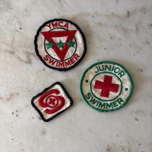 以下が含まれることがあります： 3つのヴィンテージ刺繍パッチ。 「YMCA SWIMMER」の文字と赤い三角形が入った丸いパッチ。 「JUNIOR SWIMMER」の文字と赤い十字が入った別の丸いパッチ。 3つ目のパッチは赤と白のデザインです。