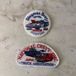 May include: Two embroidered patches. The top patch is round with a race car design and the text "Dingman Bros Racing". The bottom patch is semi-circular with a blue truck and red van design and the text "National Chevy GMC Truck Association".