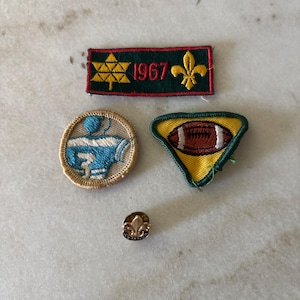 May include: A collection of three embroidered patches and one metal pin. The rectangular patch is dark green with a yellow Star of David, the year 1967, and a yellow fleur-de-lis. A circular patch shows a blue jersey, and a triangular patch features a football.
