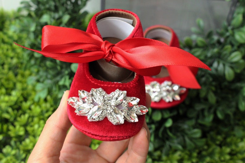 Peut inclure: Chaussures de b&eacute;b&eacute; en velours rouge avec un grand embellissement en strass et un n&oelig;ud en satin rouge.