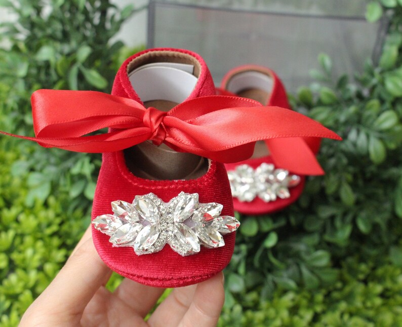 Peut inclure: Chaussures de b&eacute;b&eacute; en velours rouge avec un grand embellissement en strass et un n&oelig;ud en satin rouge.
