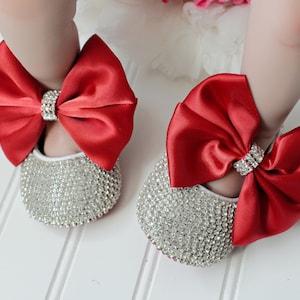 May include: A pair of baby shoes with a red satin bow and rhinestone embellishments.