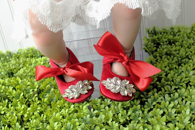 Peut inclure: Chaussures de b&eacute;b&eacute; en velours rouge avec un grand embellissement en strass et un n&oelig;ud en satin rouge.