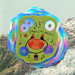 May include: A pile of holographic stickers. Each sticker has a green background with a cartoon cat wearing headphones. The text reads "I love physical media!" with musical notes and stars.